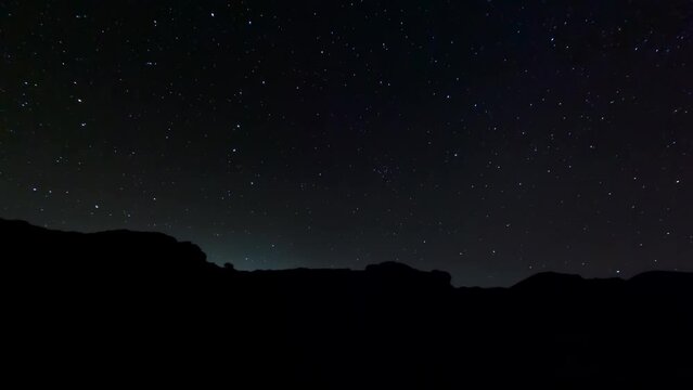 Starry nighttime time lapse with rugged landscape in silhouette in the foreground