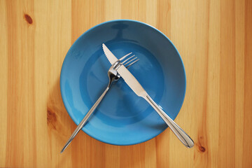 A signal "Didn't like the dish". Empty and clean blue plate with fork and knife on a wooden table as an example of table etiquette - Powered by Adobe