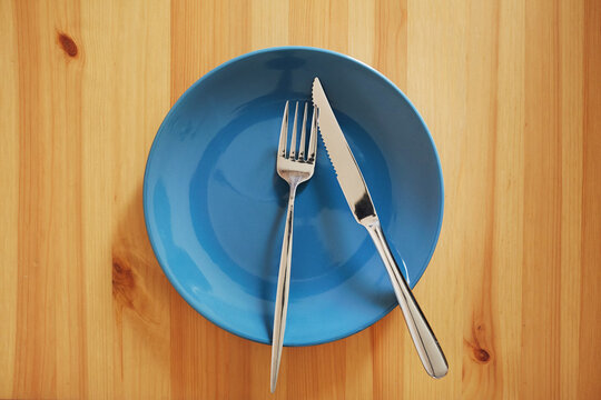 A signal "There is little food". Empty and clean blue plate with fork and knife on a wooden table as an example of table etiquette