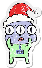 distressed sticker cartoon of a three eyed alien wearing santa hat