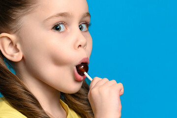 On a blue background, a girl licks a round lollipop close-up
