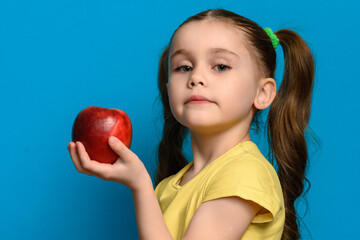 Fototapeta na wymiar The girl stands in profile on a blue background and holds a large red apple in one hand.