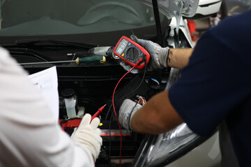 Car repairman checking and testing car battery with digital electronic tester
