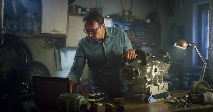 Portrait of a Man Using Laptop and Working on Fixing a Water Pump Engine in his Home Workshop. Happy Professional Male Engineer Looking at Camera, Posing, Smiling, Celebrating his Success