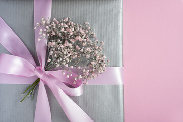 Gray gift box decorated with pink ribbon and small bouquet of gypsophila. Romantic present, pink background