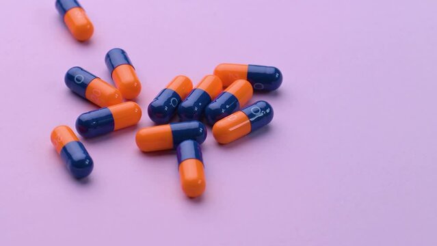 Blue and orange medicine pills dropped on a purple table