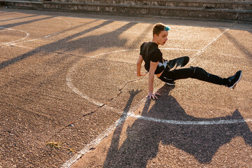 Teenage boy with blue hair breakdancing on a basketball court in the street. street dancer. youth...