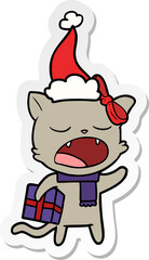 sticker cartoon of a cat with christmas present wearing santa hat