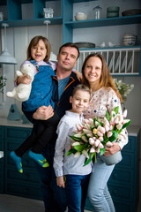 happy family  with two children holding  bouquet of white and pink spring tulips in the blue kitchen