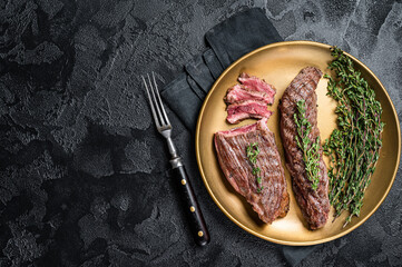 BBQ grilled Bavette Bavet beef meat steak with herbs on a plate. Black background. Top view. Copy...