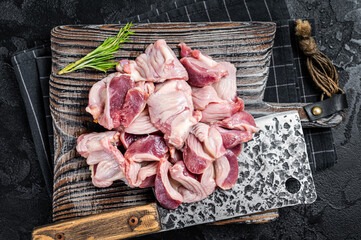 Raw chicken stomachs, giblets gizzards on a butcher board with meat cleaver. Black background. Top...