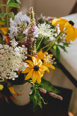 Wildflowers bouquet on background of wooden chair with white pillow in sunny rustic room. Summertime in countryside. Home simple eco decor, beautiful yellow flowers