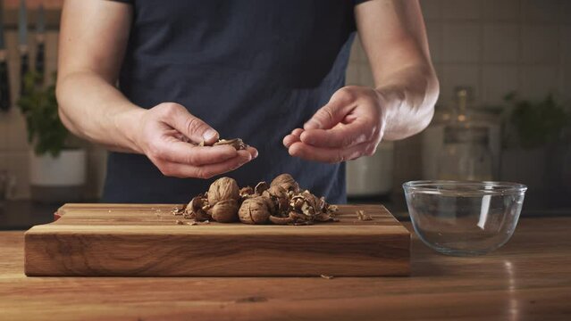 A man shelling walnuts over a wooden surface.