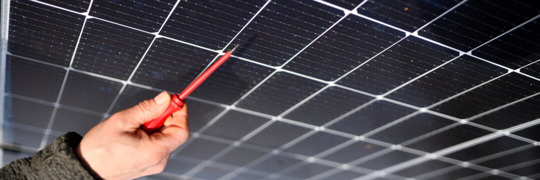 Schraubenzieher in der rechten Hand eines Solar Installateurs mit neuen, unscharfen Fotovoltaik Modulen im Hintergrund auf dem Haus Dach
