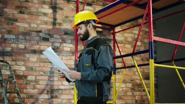 Foreman good looking guy in safety equipment and helmet looking through the plan of construction and schemes to analysing and check if everything it s okay at construction site