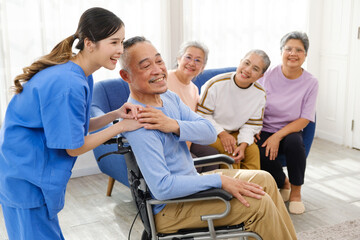 The caregiver therapist stands with an Asian senior sitting in a wheelchair with a group of senior...