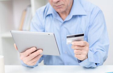Close up hands of an elderly man hold credit card and tablet computer. Online shopping