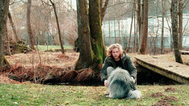 A wolf spitz and his friend. The young blonde man begins by stroking his dog and then holds both hands in the air. The dog senses the situation and wants to treat himself to the treat inside.