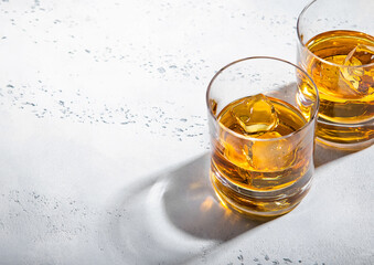 Two whiskey glasses with ice cubes on light background.