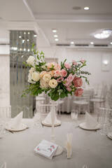 Centerpiece made of green leaves and fresh flowers stands on the dinner table. Wedding day. Fresh flowers decorations. Peony arrangements.