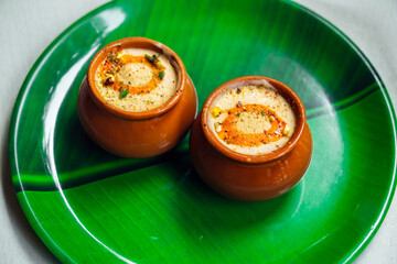 Kulfi or Qulfi ice cream in a clay pot. Kulfi is a popular traditional Indian dessert made of milk with spices and nuts. Two clay pots with ice cream on a green plate in the form of a leaf