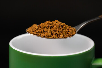 Close-up of a teaspoon with granulated instant coffee over a mug, macro.
