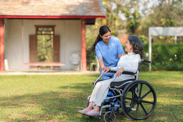 Asian nurse takes a patient in a wheelchair to make her feel refreshed and relaxed at the park.