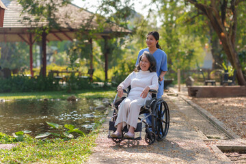 Asian nurse takes a patient in a wheelchair to make her feel refreshed and relaxed at the park.