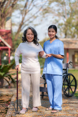 Beautiful Asian nurse taking patient walk in physiotherapy park for exercise and relaxation