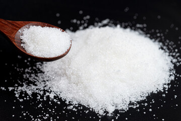 Close-up white sugar in a wooden spoon. Dark and Moody background.
