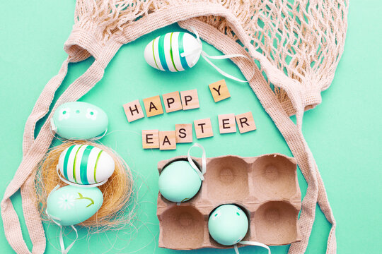 happy easter with colorful painted eggs and cotton string bag on green turquoise background