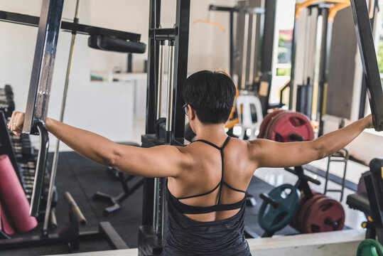 A short haired asian woman does a set of reverse pec deck flys at the gym. Sculpting and training her posterior deltoids and upper back muscles.