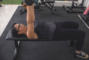 A serious forty something woman with short hair does a set of dumbbell bench presses. Working out...
