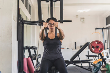 A short haired asian woman does a set of chest flys on a pec deck machine at the gym. Targeting the...