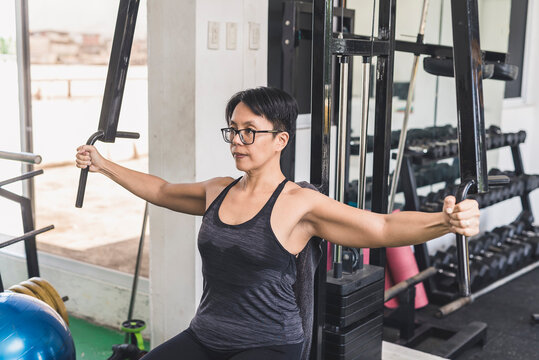A short haired asian woman does a set of chest flys on a pec deck machine at the gym. Targeting the pectoralis muscles