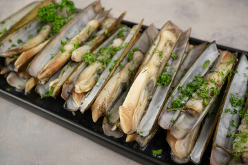 dish of razor clam grilled with garlic, parsley, olive oil and lemon slice on wood table
