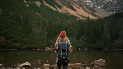 Woman traveler hipster with backpack walking near lake and looking forward at amazing mountains