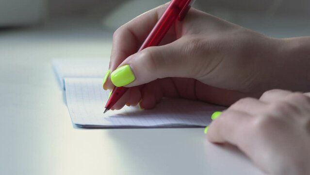 Woman hands with bright nails write down different math formulas in paper notebook at table closeup. Fingers hold red ball pen for notes