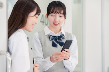 教室でスマホを見ながら話す女子高生