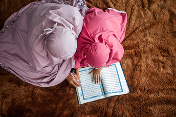 Muslim woman, a mother is teaching her daughter to read the holy book Al-Quran during the fasting...