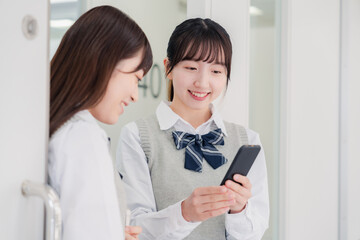 教室でスマホを見ながら話す女子高生