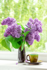 Home interior with a bouquet of blooming lilac flowers on the window.