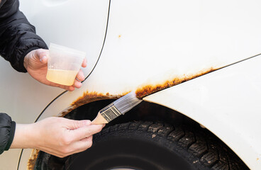 Close up view of person hand apply home use car rust stop liquid on vehicle rusty parts.