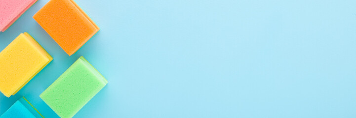 New colorful dry sponges on light blue table background. Pastel color. Closeup. Wide banner. Cleaning products. Top down view. Empty place for text.