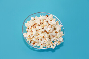 White fried popcorn in a transparent glass plate on a blue background