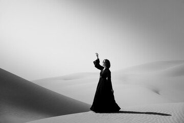 Beautiful young woman with a black abaya walking on the dunes in the desert.