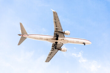 A large white passenger plane flies in the blue sky on a sunny day. Extended landing gear, bottom view