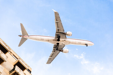 A large white passenger plane flies in the blue sky low over a residential building on a sunny day....