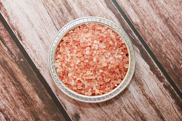 Obraz na płótnie Canvas Natural pink Himalayan salt in a decorative plate on a brown wooden background