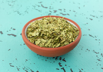 Cut tarragon in a small terracotta bowl on a mottled tabletop side view.